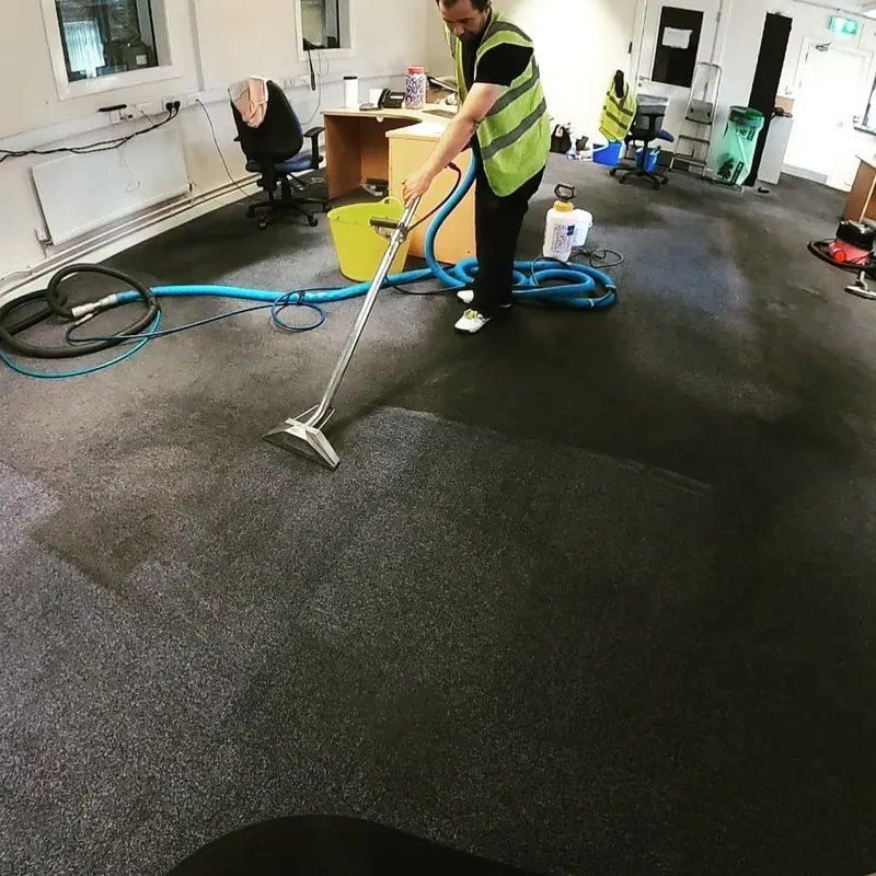 Technician in a high-visibility vest cleaning an office carpet with a floor wand
